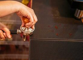 Hand of a barista holding a portafilter and a coffee tamper making an espresso coffee. Barista presses ground coffee using a tamper in a coffee shop photo