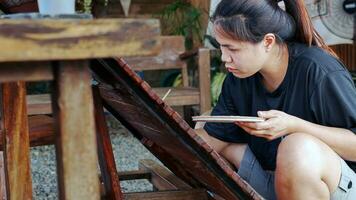 Asian woman painter creating art use a paintbrush to draw lettering designs on a wooden coffee shop sign. outdoor activities, People doing activities. photo