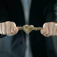 A heart-shaped knot. The businessman's hands tighten the rope knot against background of suit in blur. The concept of feeling. photo