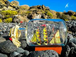 a bottle with a sailboat inside on a rocky beach photo