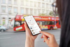 City Sightseeing app on smartphone in woman hands. City tourist bus in background photo