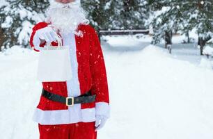 Santa Claus outdoor in winter and snow handing in hand paper bags with craft gift, food delivery. Shopping, packaging recycling, handmade, delivery for Christmas and New year photo