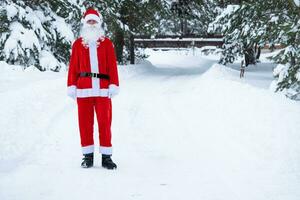 Santa Claus is stands on a snowy fairy-tale road outdoor in winter with pine trees. Celebrating Christmas and New Year. photo