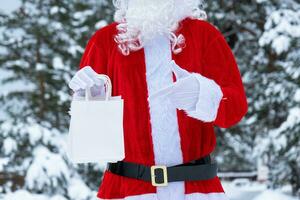 Santa Claus outdoor in winter and snow handing in hand paper bags points with his finger. Shopping, packaging recycling, handmade, delivery for Christmas and New year photo