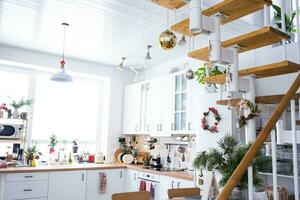 festivo Navidad decoración en blanco cocina, blanco moderno desván interior con un metal modular escalera con de madera pasos. nuevo año, ánimo, acogedor hogar. foto