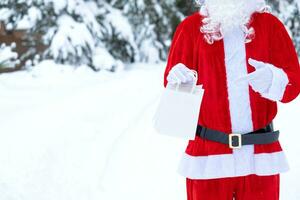 Papa Noel claus al aire libre en invierno y nieve entrega en mano papel pantalones puntos con su dedo. compras, embalaje reciclaje, hecho a mano, entrega para Navidad y nuevo año foto