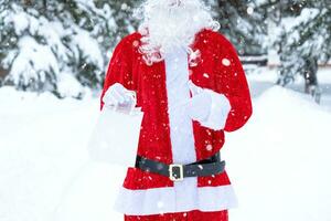 Papa Noel claus al aire libre en invierno y nieve entrega en mano papel pantalones puntos con su dedo. compras, embalaje reciclaje, hecho a mano, entrega para Navidad y nuevo año foto