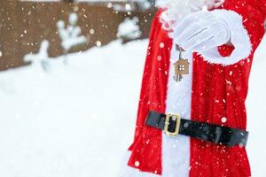 House key with keychain cottage in hands of Santa Claus outdoor in snow. Deal for real estate, purchase, construction, relocation, mortgage. Cozy home. Merry Christmas, new year booking event and hall photo