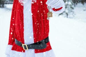 House key with keychain cottage in hands of Santa Claus outdoor in snow. Deal for real estate, purchase, construction, relocation, mortgage. Cozy home. Merry Christmas, new year booking event and hall photo
