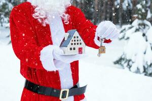 House key with keychain cottage in hands of Santa Claus outdoor in snow. Deal for real estate, purchase, construction, relocation, mortgage. Cozy home. Merry Christmas, new year booking event and hall photo