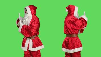 Father christmas pushing something aside, pretending to reject a big object in studio with greenscreen backdrop. Young man portraying santa claus doing dismiss symbol left or right. photo