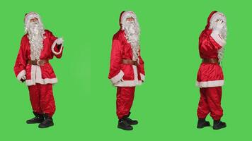 Santa claus doing gesture with hands, calling someone to come over and accompany him. Saint nick character in suit hailing person to join, full body greenscreen backdrop studio. photo