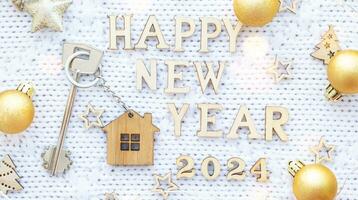 House key with keychain cottage on cozy festive knitted background with stars, bokeh. Happy New Year 2024 wooden letters, greeting card. Purchase, construction, relocation, mortgage, insurance photo