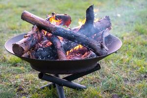 Metal fire bowl with burning wood in the yard. Safe decorative fire pit photo