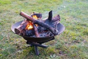 Metal fire bowl with burning wood in the yard. Safe decorative fire pit photo