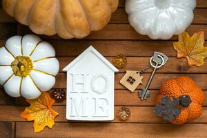 Cozy layout on a wooden background of slats with pumpkins, autumn leaves, a house and keys - autumn mood, Halloween, housing, relocation, mortgage, insurance. photo