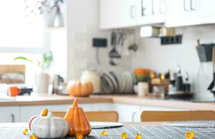 Decor of white classic kitchen with pumpkins, garlands, latern for Halloween and harvest with figurine of house. Autumn mood in home interior, modern loft style. real estate, insurance, mortgage photo