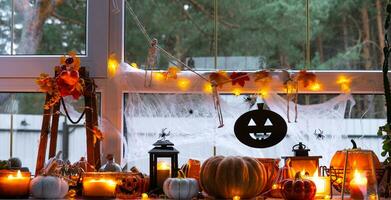 Festive decor of the house on the windowsill for Halloween - pumpkins, Jack o lanterns, skulls, cobwebs, spiders, skeletons, candles and a garland - a cozy and terrible mood photo