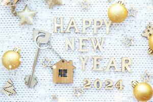 House key with keychain cottage on cozy festive knitted background with stars, bokeh. Happy New Year 2024 wooden letters, greeting card. Purchase, construction, relocation, mortgage, insurance photo