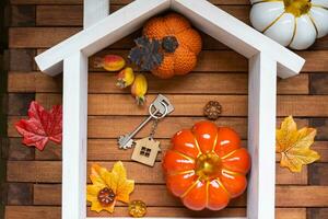 Cozy layout on a wooden background of slats with pumpkins, autumn leaves, a house and keys - autumn mood, Halloween, housing, relocation, mortgage, insurance. photo