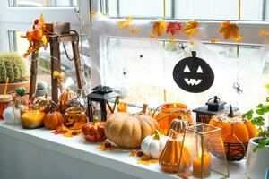 Festive decor of the house on the windowsill for Halloween - pumpkins, Jack o lanterns, skulls, cobwebs, spiders, skeletons, candles and a garland - a cozy and terrible mood photo