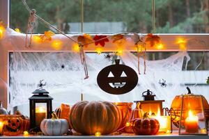 Festive decor of the house on the windowsill for Halloween - pumpkins, Jack o lanterns, skulls, cobwebs, spiders, skeletons, candles and a garland - a cozy and terrible mood photo