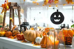 Festive decor of the house on the windowsill for Halloween - pumpkins, Jack o lanterns, skulls, cobwebs, spiders, skeletons, candles and a garland - a cozy and terrible mood photo