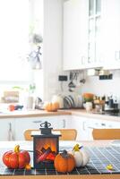 Decor of white classic kitchen with pumpkins, garlands, latern for Halloween and harvest with figurine of house. Autumn mood in home interior, modern loft style. real estate, insurance, mortgage photo