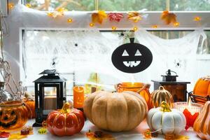 Festive decor of the house on the windowsill for Halloween - pumpkins, Jack o lanterns, skulls, cobwebs, spiders, skeletons, candles and a garland - a cozy and terrible mood photo