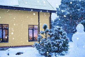 acogedora ventana festiva de la casa exterior con la cálida luz de las guirnaldas de luces de hadas en el interior: celebre la navidad y el año nuevo en un hogar cálido. árbol de navidad, bokeh, nieve en pinos y nevadas foto