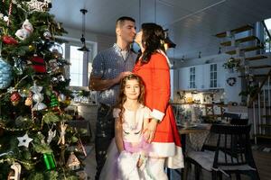 A traditional family of mom, dad and daughter near the Christmas tree in the interior of their house. Celebrating the New year with your family photo