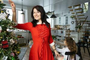 Woman in a red Santa dress and a daughter in a home interior with a Christmas tree and New Year decor. Preparation for the holidays, party photo