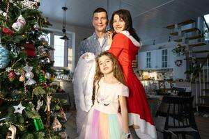 A traditional family of mom, dad and daughter near the Christmas tree in the interior of their house. Celebrating the New year with your family photo