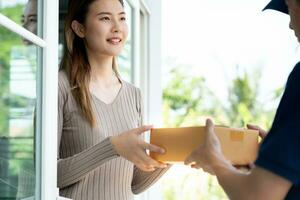 Happy smiling woman receives boxes parcel from courier in front house. Delivery man send deliver express. online shopping, paper containers, takeaway, postman, delivery service, packages photo