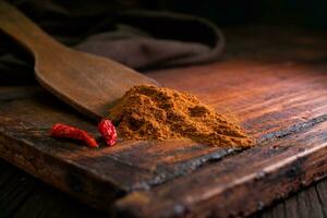 Spicy minced delicious seasoning with red dried chilli peppers on a wooden spatula with a wooden board in a dark background photo