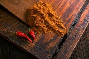 Delicious spicy ground seasoning with red dried peppers on a wooden brown table photo