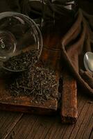 Delicious dried loose leaf tea spilled from glass jar on wooden table on dark background photo