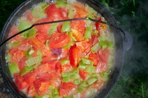 The process of cooking outdoors. Vegetables in a cauldron on a fire. Top view. photo