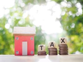 Wooden blocks with the word TAX on stack of coins and miniature house. The concept of payment tax for house, Property investment, House mortgage, Real estste. photo