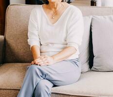 An Asian senior grandparents is sitting on sofa and using a remote control to watch television together. The elderly female want to watch comedy game show, so she tell her husband to switch channel. photo