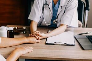 Doctor giving hope. Close up shot of young female physician leaning forward to smiling elderly lady patient holding her hand in palms. Woman caretaker in white coat supporting encouraging old person photo