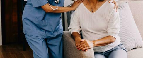 Happy young female nurse provide care medical service help support smiling old grandma at homecare medical visit, lady carer doctor give empathy encourage retired patient sit on sofa at home hospital photo