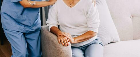 Happy young female nurse provide care medical service help support smiling old grandma at homecare medical visit, lady carer doctor give empathy encourage retired patient sit on sofa at home hospital photo