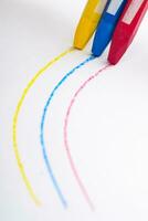 three colored crayon sticks draw lines forming a curve on white paper photo