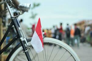 The front of the antique bicycle has an Indonesian flag with a blurred background photo