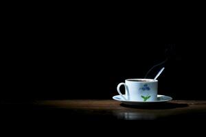 un taza de caliente café elaborada con un cuchara en un de madera mesa en un negro antecedentes foto