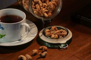 a bunch of cashews spilled from a jar on the table with a cup of tea photo