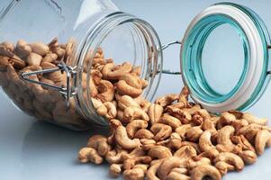 a bunch of cashews in a jar that fell and ended up spreading on the white table photo