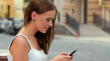 lado Visão do uma moda mulher usando uma Smartphone sentado em uma Banco dentro a rua video