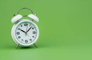 White alarm clock tells time working with time importance of time punctuality White clock on a green background photo